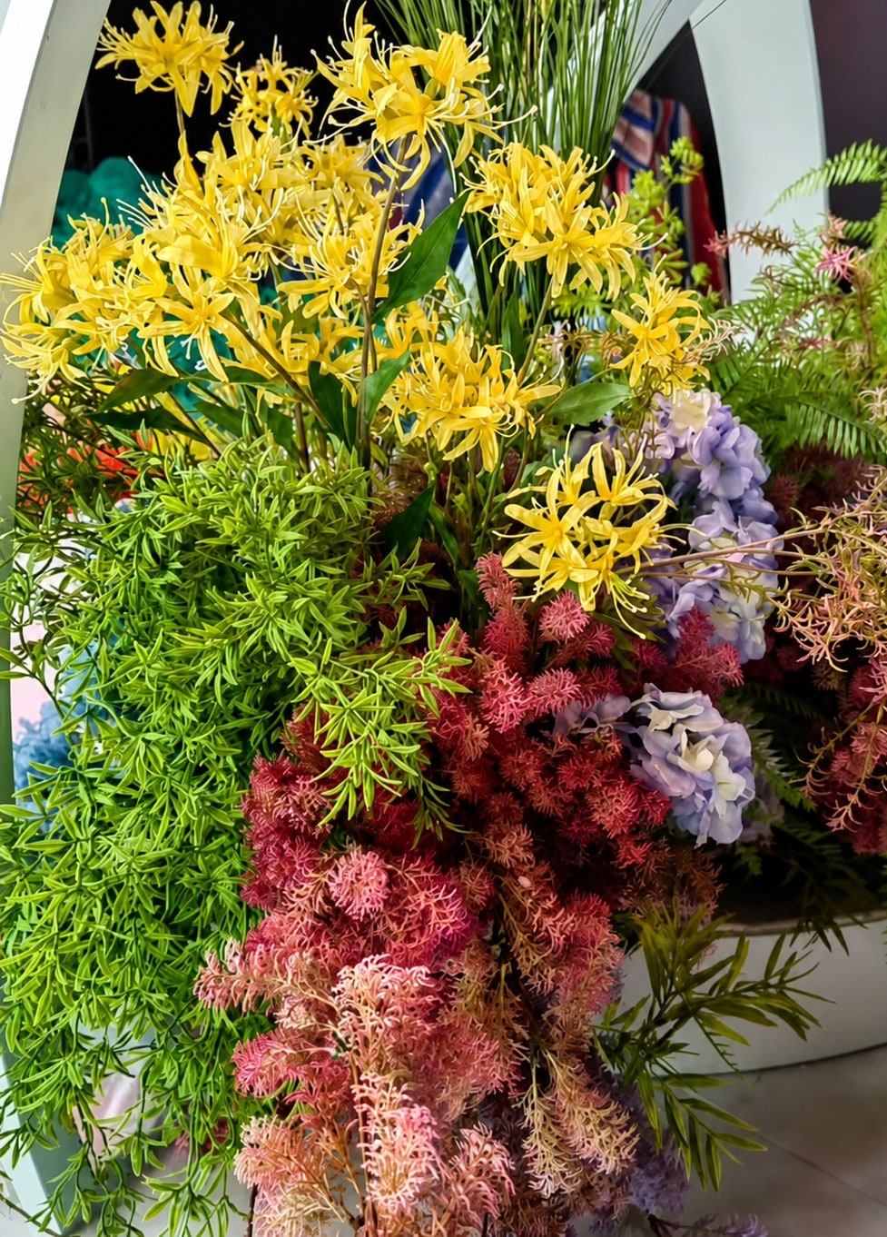 黃色石蒜與紫藍繡球、粉紅羽狀花材交織的近景，襯著白色拱形結構