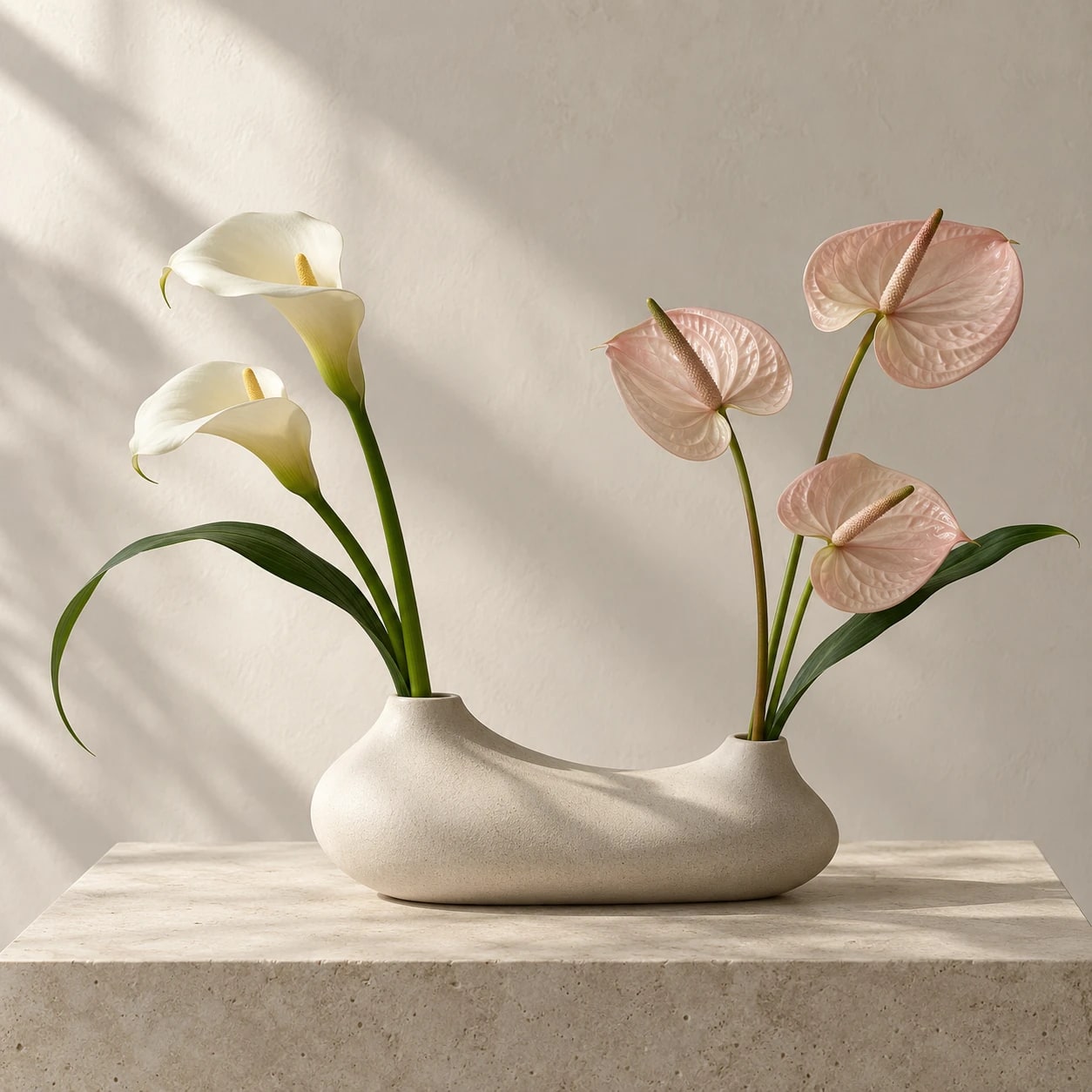 米白石材花器插著白色海芋與粉色火鶴,擺在石台上,後方米色牆面映著斜光