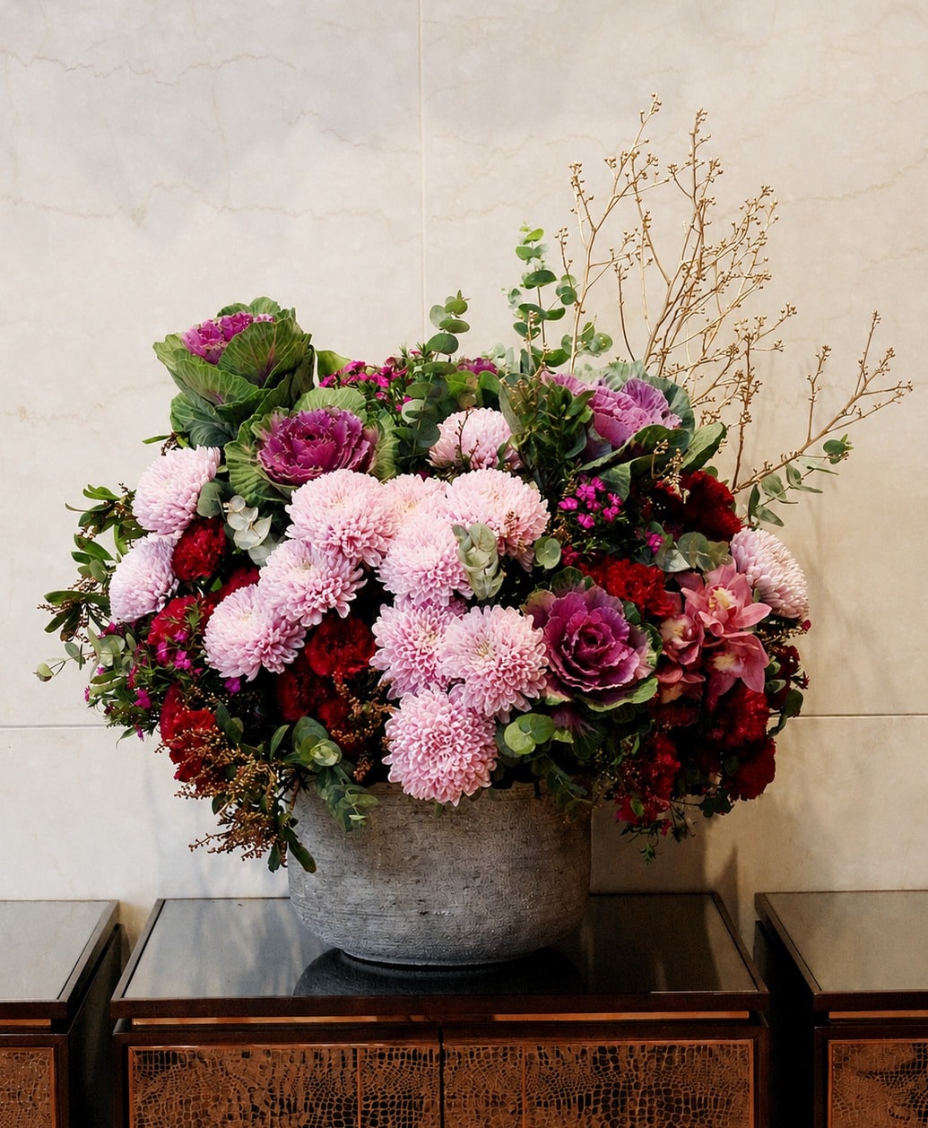 米色石牆前的水泥缽花藝,粉色菊花、紫色羽衣甘藍與暗紅色花材層層堆疊